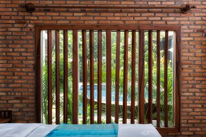 Una habitación con pared de ladrillo, ventana con persianas verticales y cama con cubrecama azul.