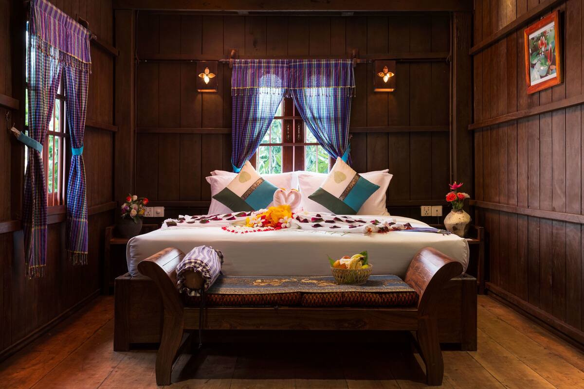Ein Zimmer mit Holzwänden, einem Bett, einer Bank und einem kleinen Tisch mit Blumen.