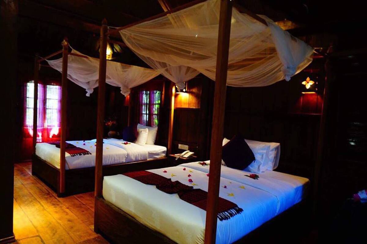 Ein Zimmer mit vier Betten, jedes mit einem Baldachin. Holzdielen und ein Fenster mit Buntglas.