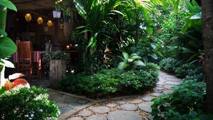 Un sentier de jardin menant à une table et des chaises en bois rustique, le tout entouré d’une végétation luxuriante et de jardinières suspendues.