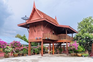 A traditional wooden house with a balcony, surrounded by potted plants and flowers. - Athithara Homestay (Ayutthaya)