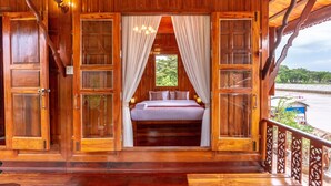 A wooden room with a bed, curtains, and a view of greenery. - Athithara Homestay (Ayutthaya)