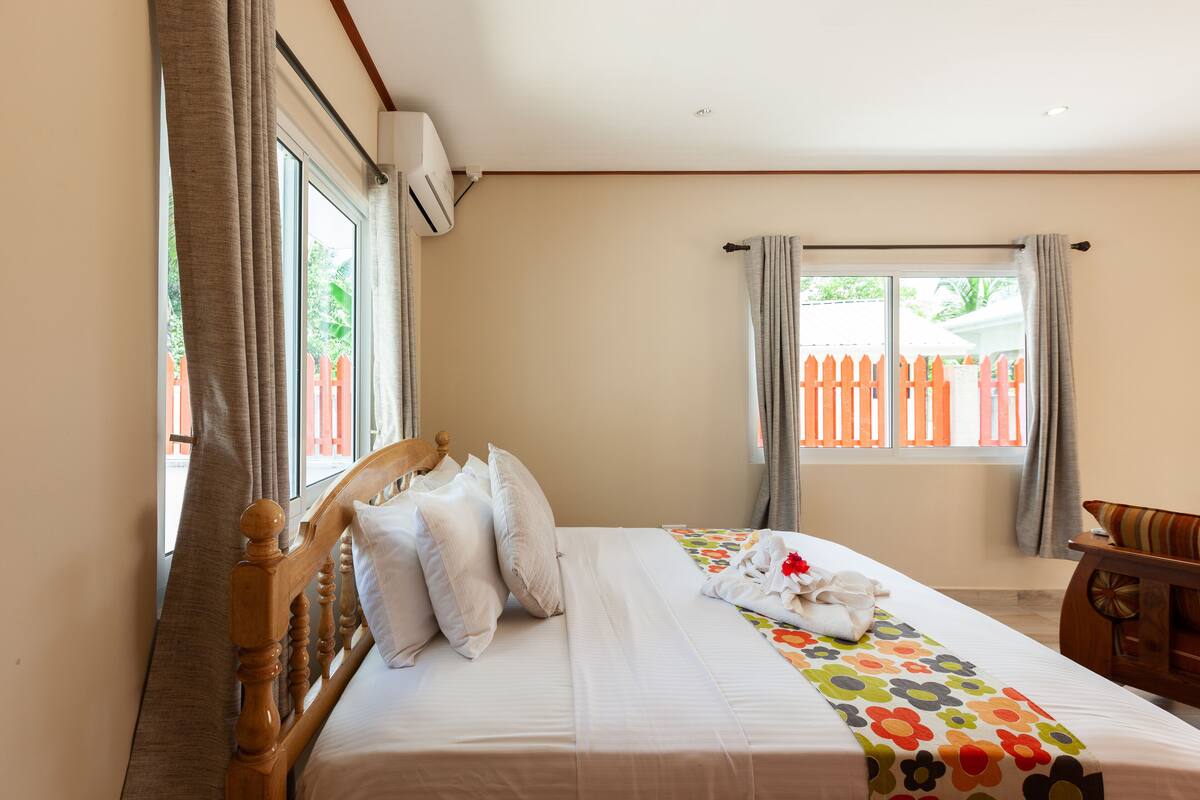 A neatly made bed with a floral bedspread, a wooden headboard, and a window with curtains.