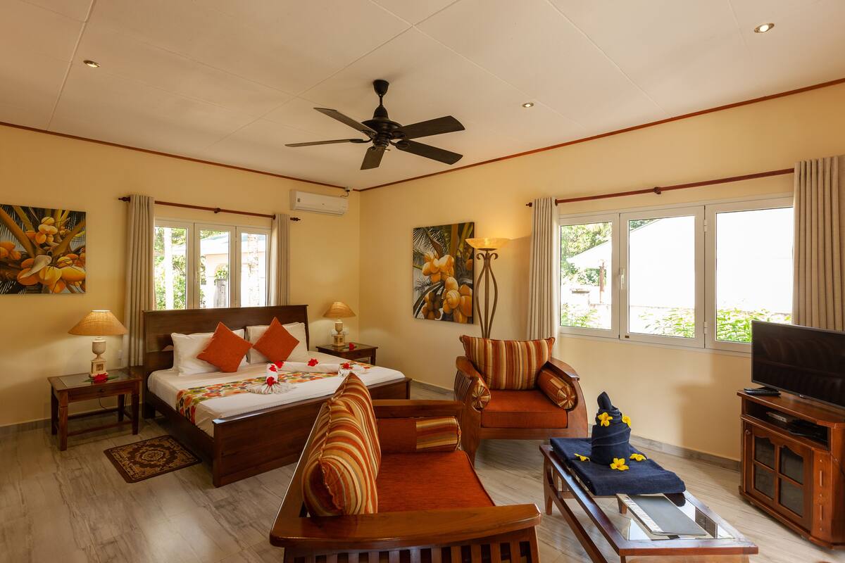 A hotel room with a bed, a sofa, a TV, and a ceiling fan.