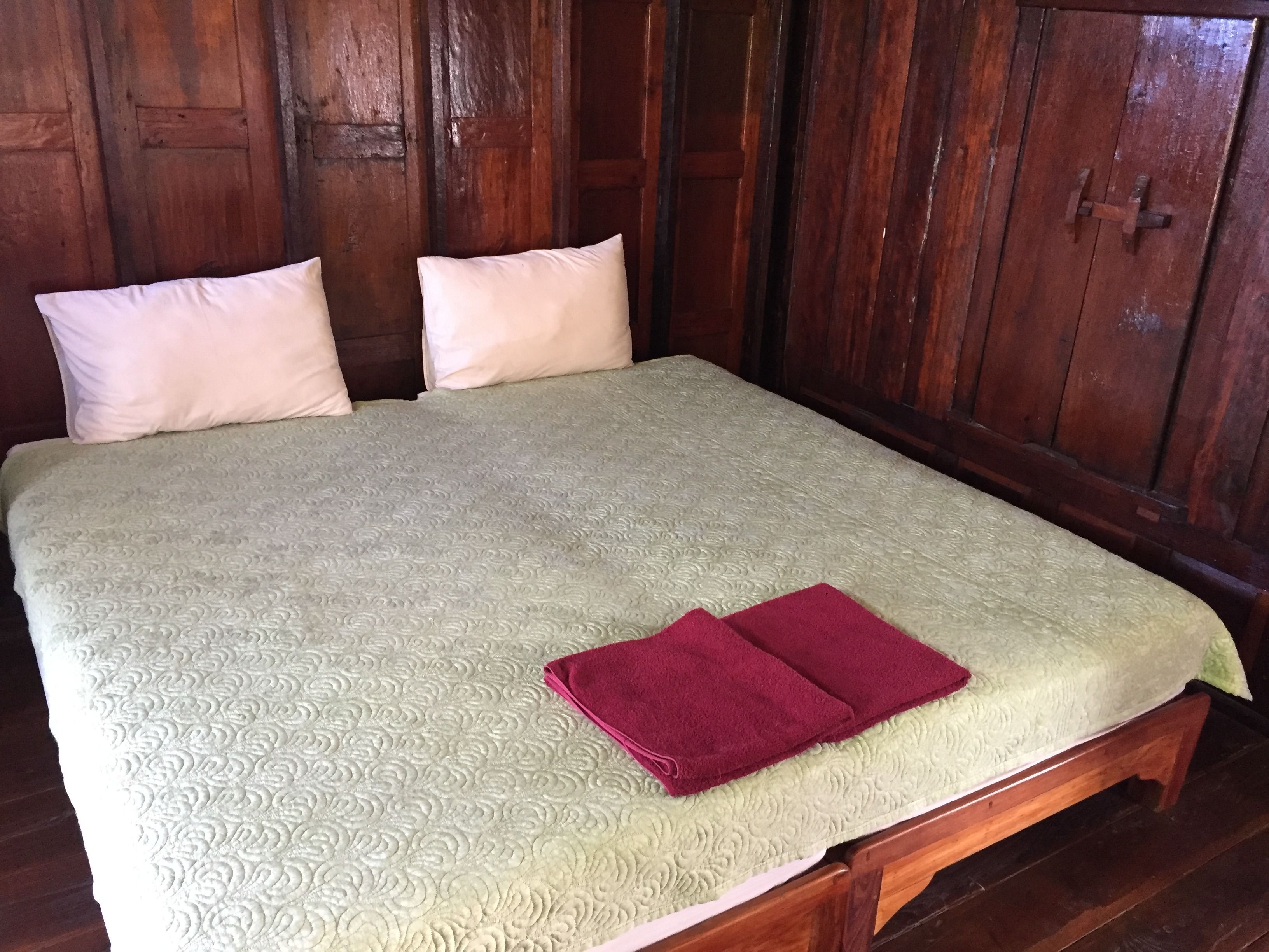 Una cama con cubierta acolchada y dos almohadas, cabecera de madera y suelo de madera.
