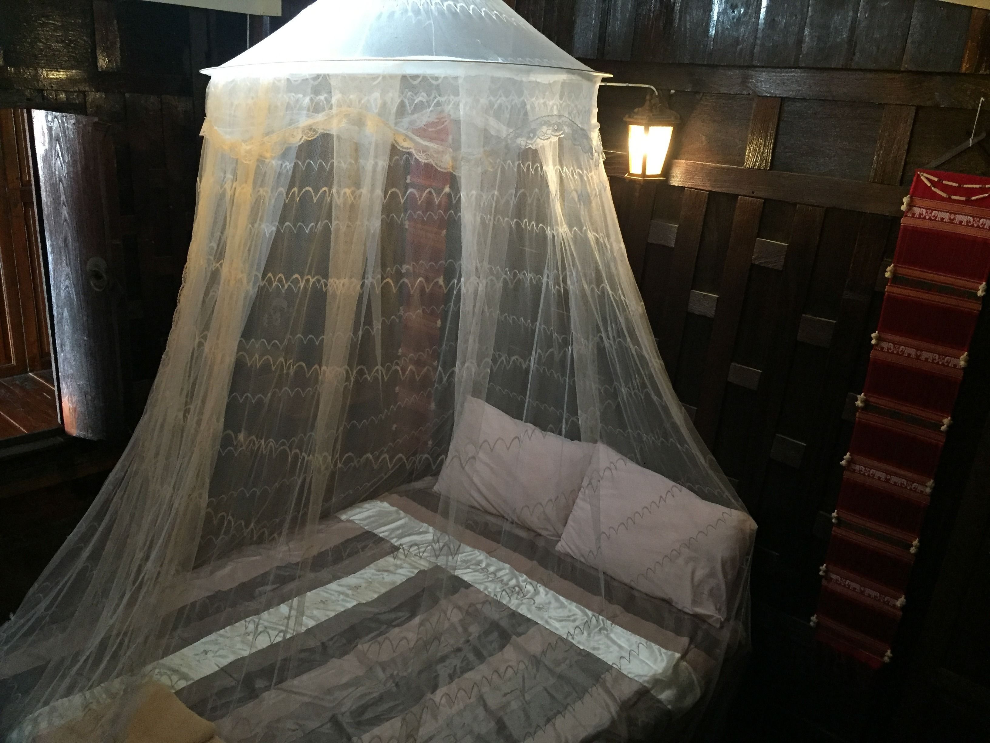A bed with a canopy and pillows, a wall-mounted lantern, and a patterned rug.