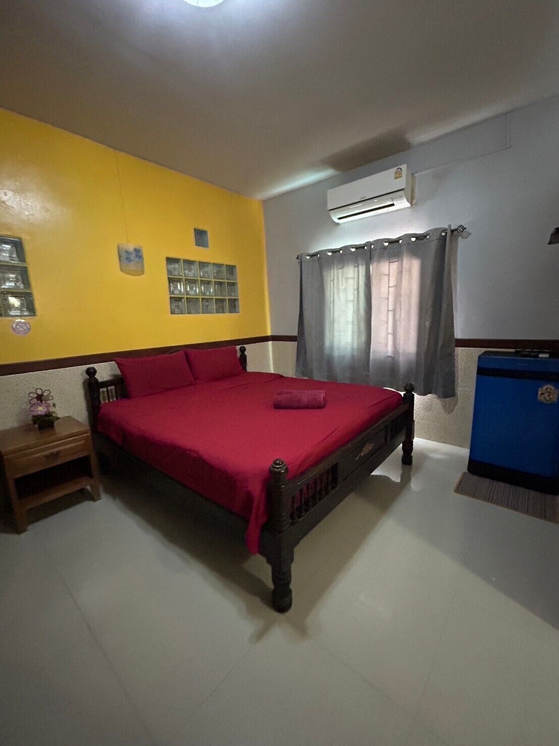 A bedroom with a bed, a nightstand, a window with curtains, and an air conditioning unit.
