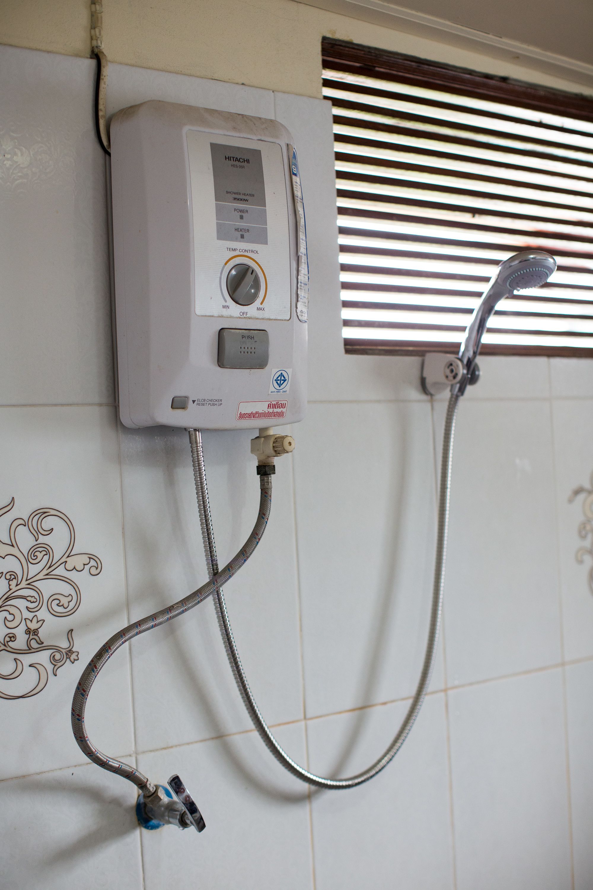 A wall-mounted water heater with control panel, connected to a showerhead and hose.