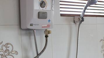 A wall-mounted water heater with control panel, connected to a showerhead and hose.