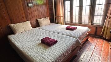 A room with two beds, wooden walls, a window with curtains, and an air conditioning unit.