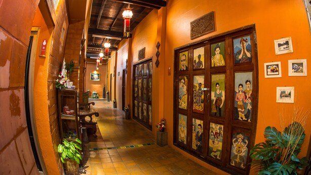 A corridor with wooden doors, framed artwork, and potted plants. - Baan Are Gong Riverside Homestay (Ayutthaya)