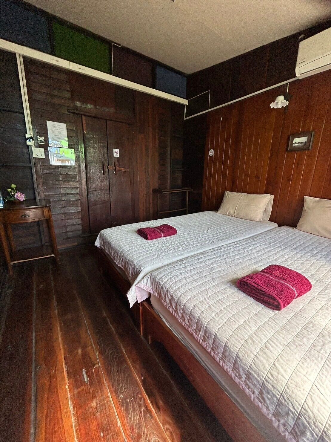 A bedroom with two beds, wooden flooring, a wardrobe, and a small table with a vase.