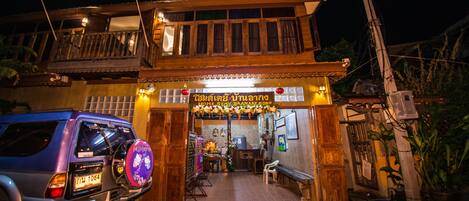 A traditional wooden house with a balcony, a signboard, and a parked car.