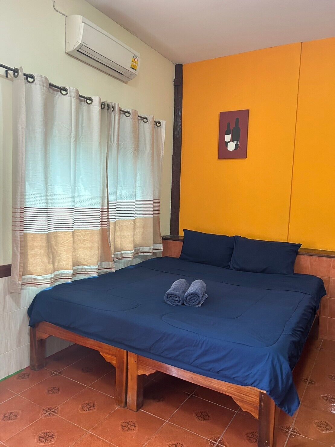Ein Schlafzimmer mit Bett, Vorhängen, einer Klimaanlage und einem an der Wand hängenden Bild.