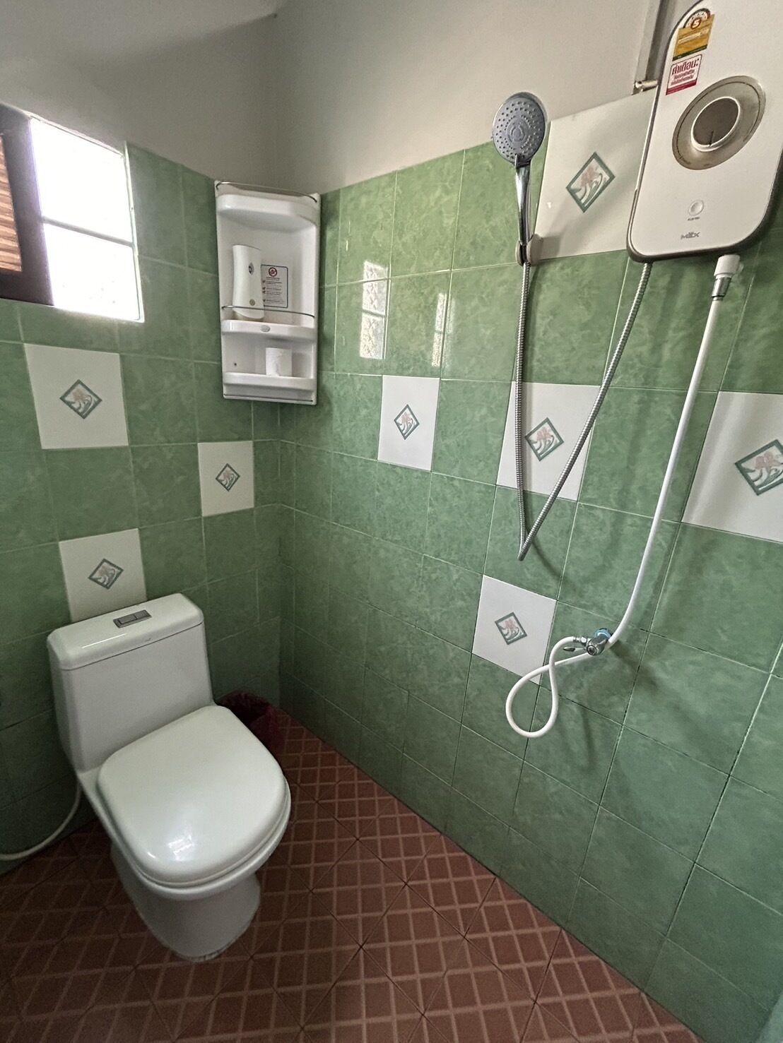 Un baño con inodoro, ducha y paredes con azulejos verdes.