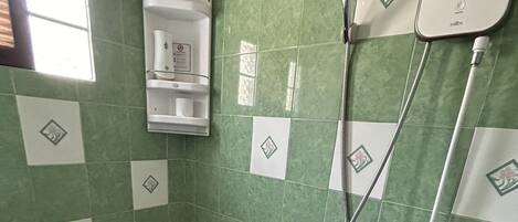 Un baño con inodoro, ducha y paredes con azulejos verdes.