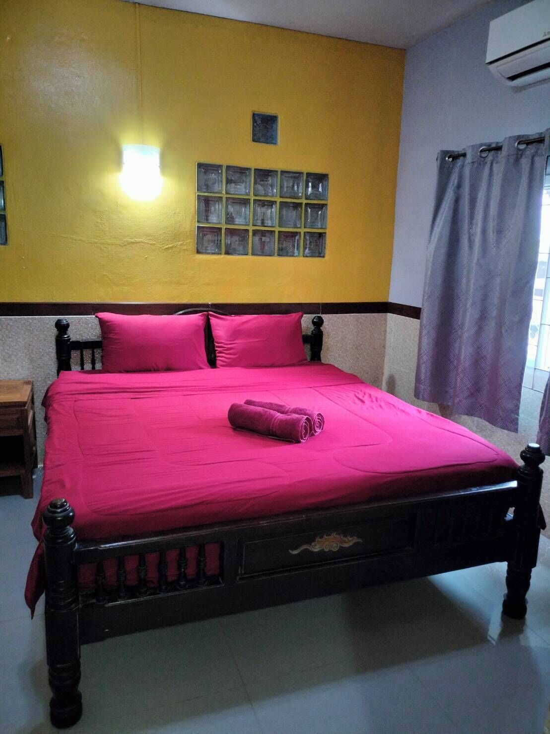 Un letto con una coperta e dei cuscini rosa acceso, una testiera in legno e una finestra con tende.