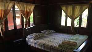 Una cama con estructura de madera, una colcha y almohadas a cuadros, una mesita de noche y cortinas en dos ventanas.