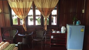 Una habitación acogedora con dos sillones de mimbre, una mesita, una cama con colcha de cuadros, un refrigerador azul y una estantería con una tetera y tazas.