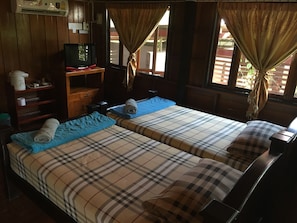 Une chambre avec deux lits, un bureau en bois, une télévision et une fenêtre avec des rideaux.