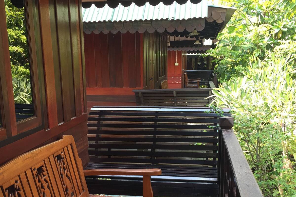 A wooden bench with intricate carvings, a metal railing, and a view of a traditional building with a tiled roof.