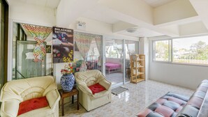 A spacious living area with a sofa, two armchairs, a coffee table, and a large window offering a view of the outside. - Bann One Love (Ayutthaya)