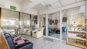 A hotel lobby with a sofa, a bookshelf, and a sliding glass door leading to another room. - Bann One Love (Ayutthaya)