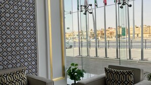A hotel lobby with a patterned wall, a large mirror, and a view of the street outside. - Sama Inn Hotel (Riyadh)