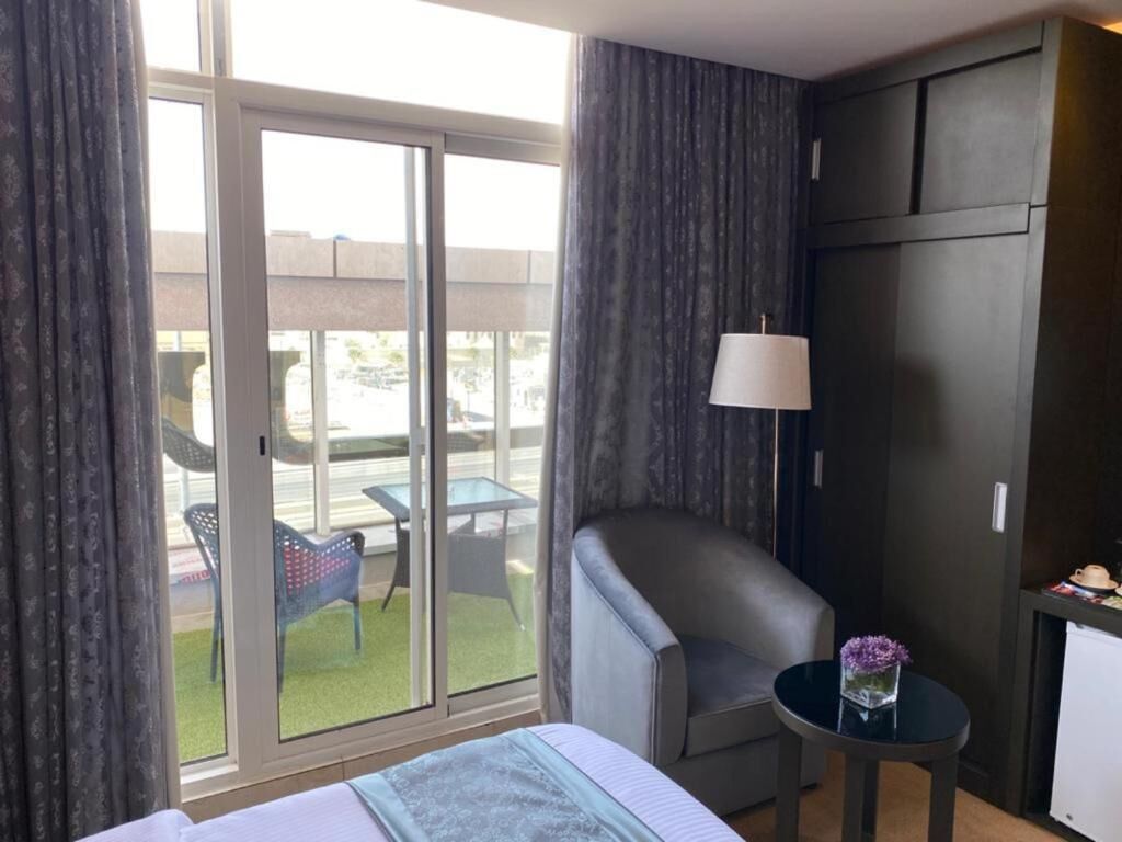 Habitación de hotel con cama, una silla, una mesita con lámpara y vistas a un espacio exterior con mesa y sillas.