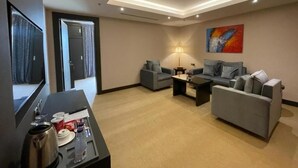 A modern hotel room with a flat-screen TV, two grey sofas, a coffee table, and a painting on the wall. - Sama Inn Hotel (Riyadh)
