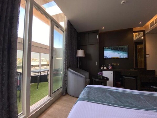 A hotel room with a bed, a TV, a desk, and a balcony with a table and chairs. - Sama Inn Hotel (Riyadh)