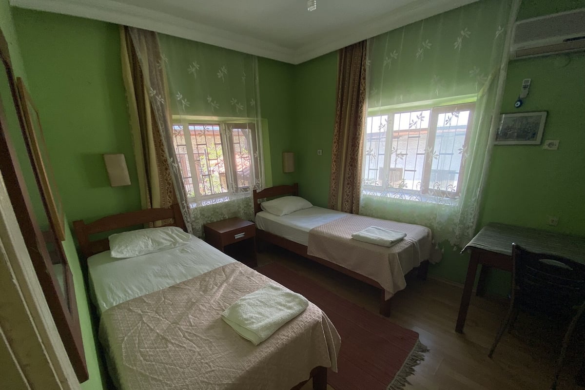 Habitación con dos camas individuales, un escritorio de madera y una ventana con cortinas.