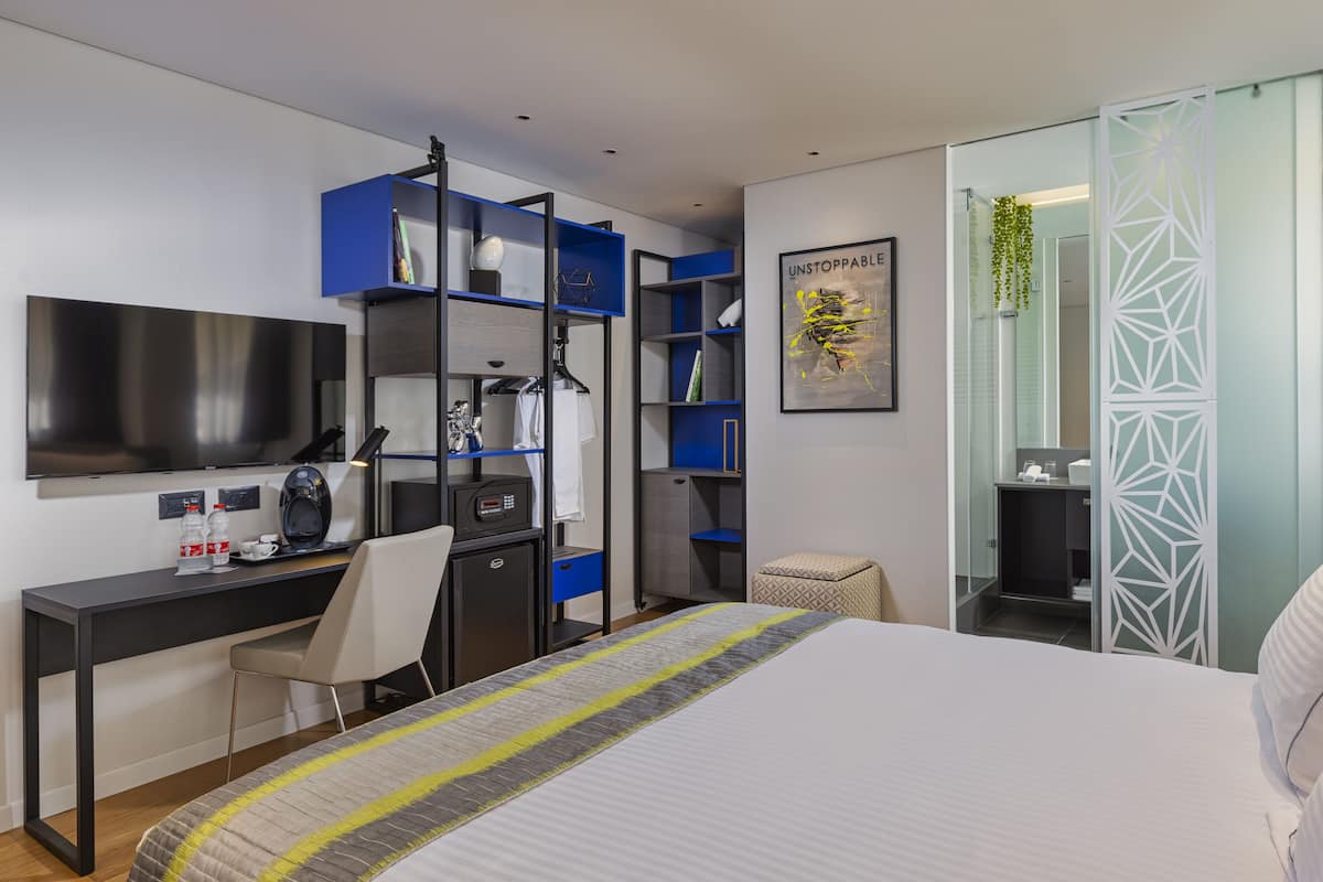 Ein modernes Hotelzimmer mit Bett, Schreibtisch und integriertem Bücherregal.