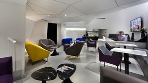 Ein modernes Interieur mit verschiedenen Sitzgelegenheiten, darunter ein gelber Sessel, ein schwarzer Marmortisch und eine Rezeption mit Theke und Bildschirm.