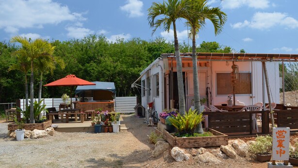 A mobile home with outdoor seating, surrounded by potted plants and a gravel path. - Guest house ISA (Motobu)