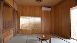 A traditional Japanese room with tatami flooring, a shoji screen, a wooden table, and an air conditioning unit. - Guest house ISA (Motobu)