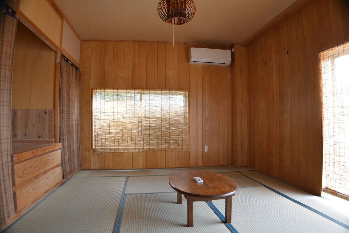 A traditional Japanese room with tatami flooring, a shoji screen, a wooden table, and an air conditioning unit.