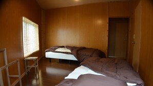 A room with two beds, wooden walls, a window with blinds, and a door. - Guest house ISA (Motobu)