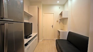 A compact living space with a kitchenette, a black sofa, and a television on a white cabinet.