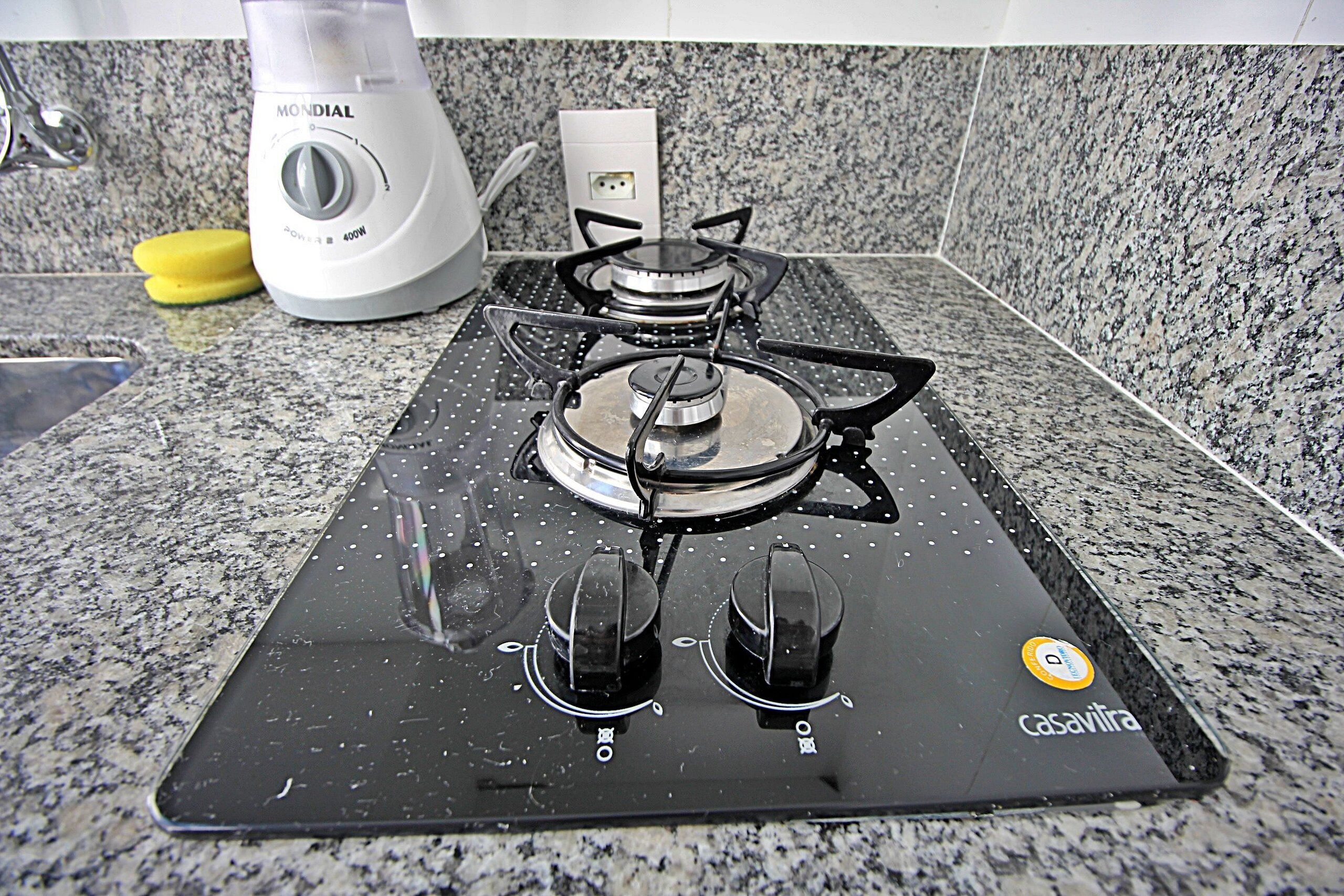 A kitchen with a black gas stove, a white electric kettle, and a granite countertop.