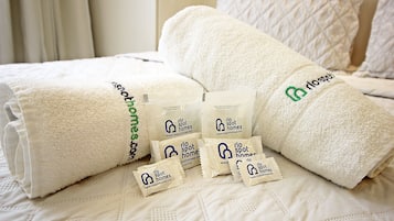 Cama bem arrumada com lençóis brancos e vários pequenos frascos de produtos de higiene pessoal.