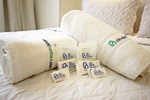 A neatly made bed with white linens and several small packets of toiletries.