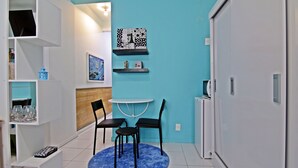 A compact living space with a blue accent wall, a small round table with chairs, a white cabinet, and shelves with various items. - Rio Spot Apartment C019 (Rio de Janeiro)