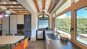 A modern kitchen with wooden beams, a large window, and a dining area with colorful chairs. - Palm Tree Villa (Seogwipo)