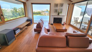 A modern living room with a wooden ceiling, large windows, a fireplace, and a seating area. - Palm Tree Villa (Seogwipo)