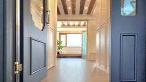 A hallway with a wooden ceiling, a blue door, and a bed with a plant in the background. - Palm Tree Villa (Seogwipo)