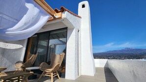 A balcony with wicker chairs, a table, and a view of a mountain. - Palm Tree Villa (Seogwipo)