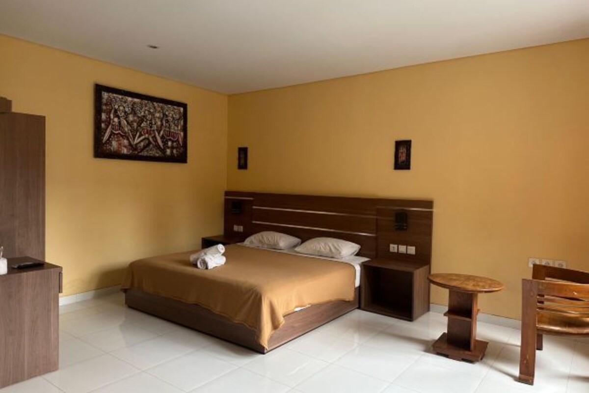 Una habitació d'hotel amb un llit, una taula petita, una cadira i un quadre a la paret.