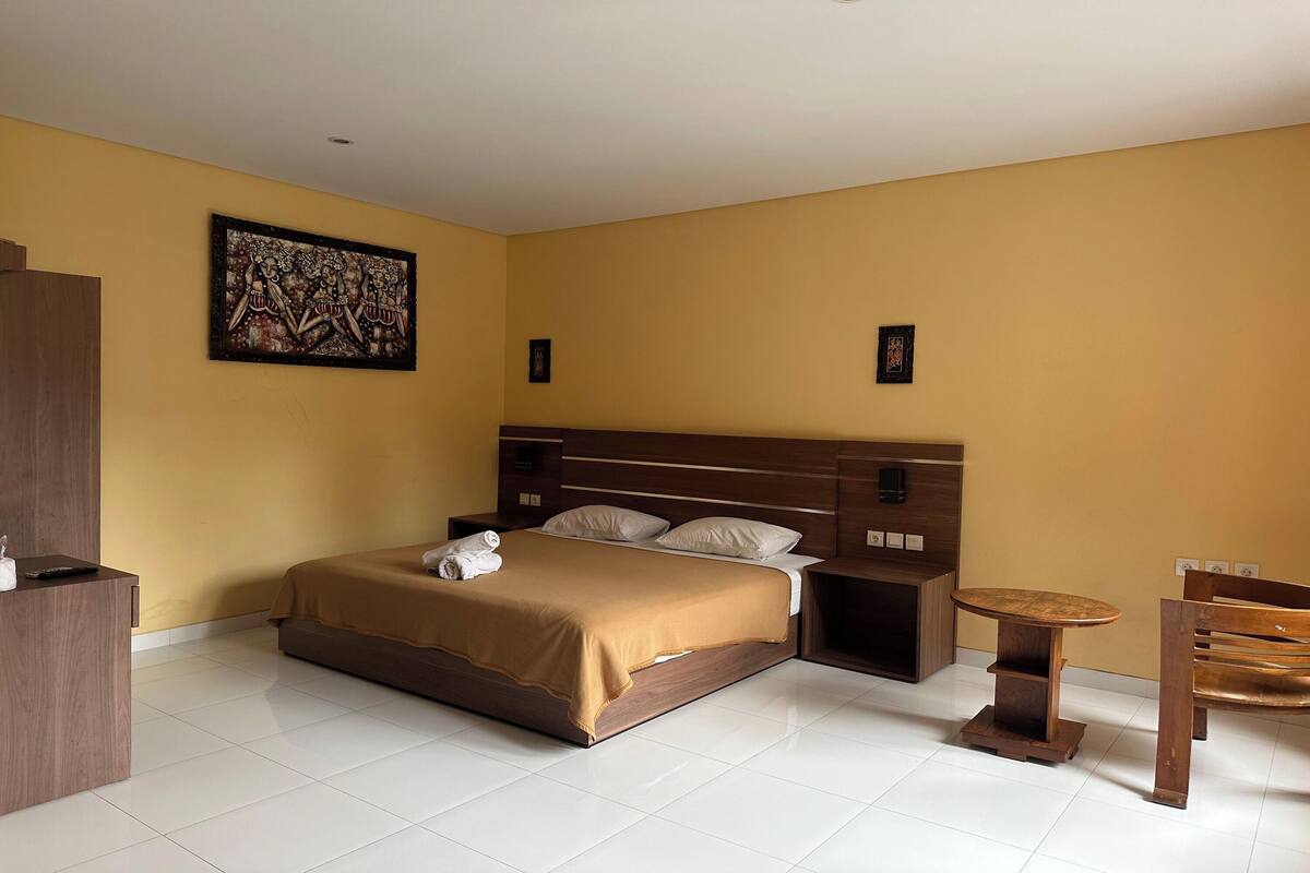 A hotel room with a bed, a wooden nightstand, a small round table, and a chair.