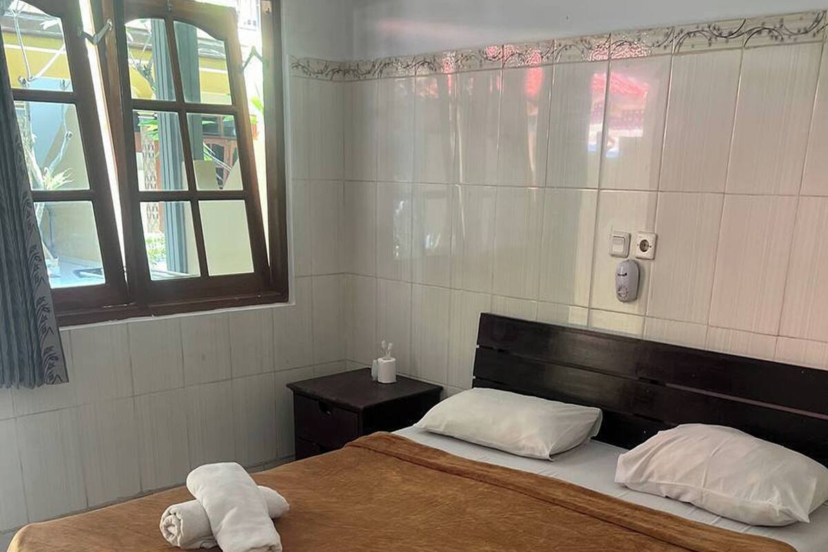 A hotel room with a bed, a nightstand, a window with a view, and a tiled floor.